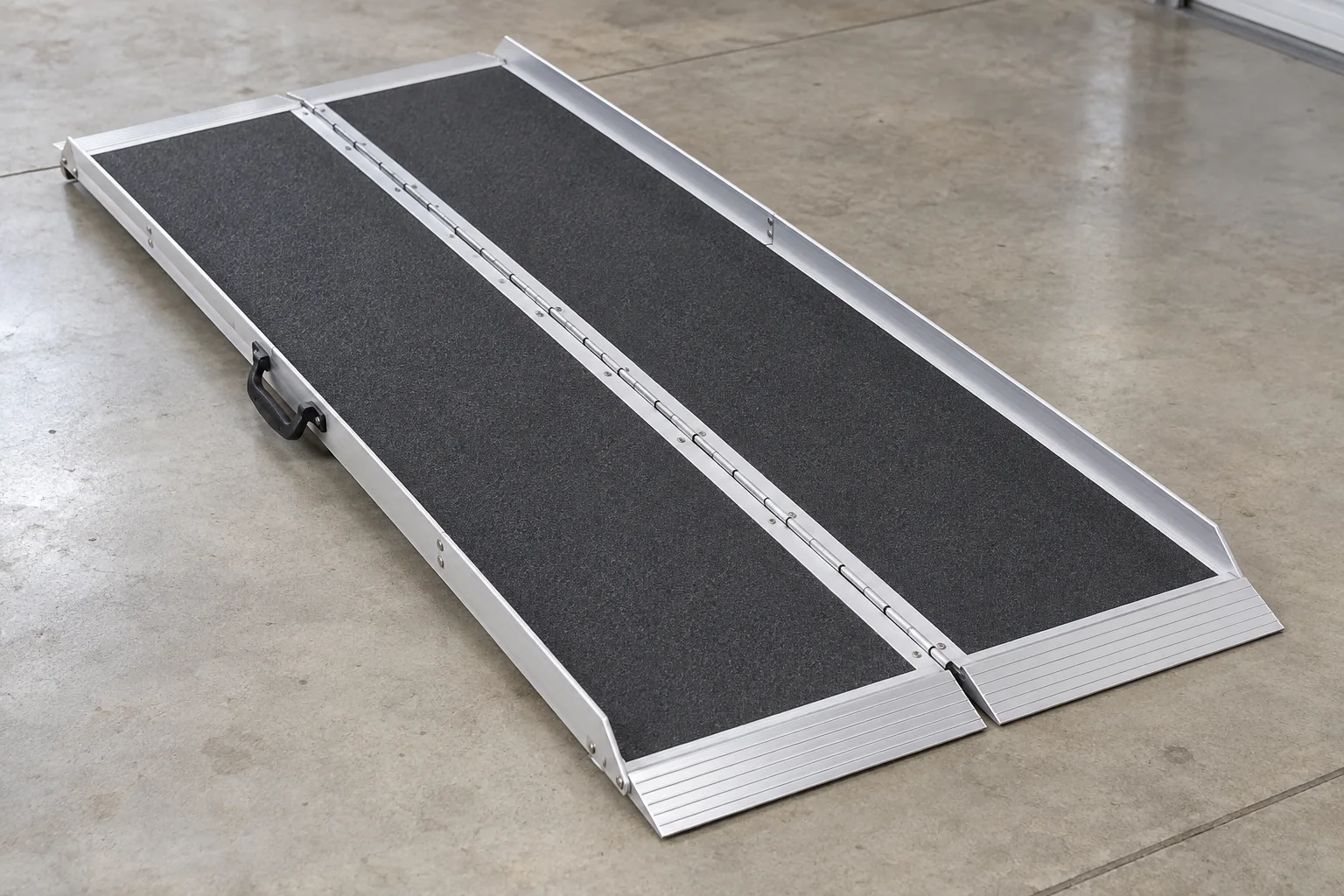 Unfolded aluminum wheelchair ramp with dark textured panels lying flat on a concrete floor